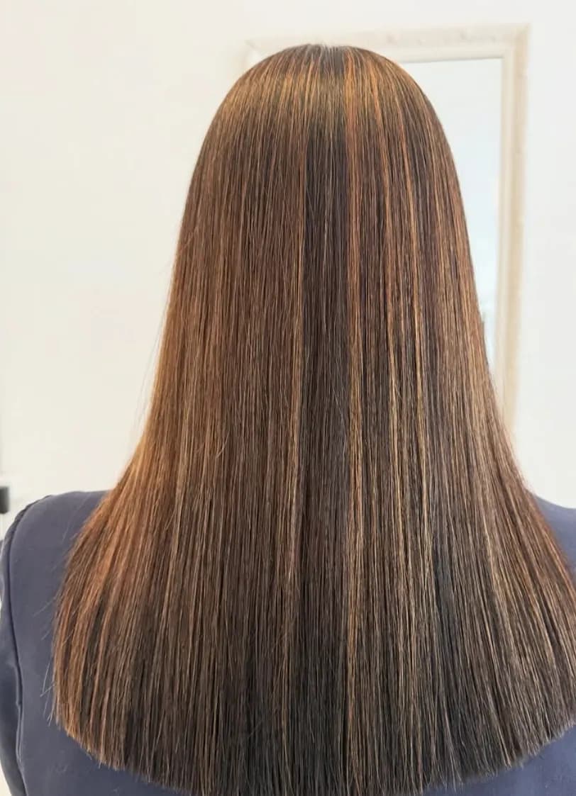 Dunkelbraunes Haar mit warmen kupferfarbenen Straehnen, glatt bis zur Schulter.