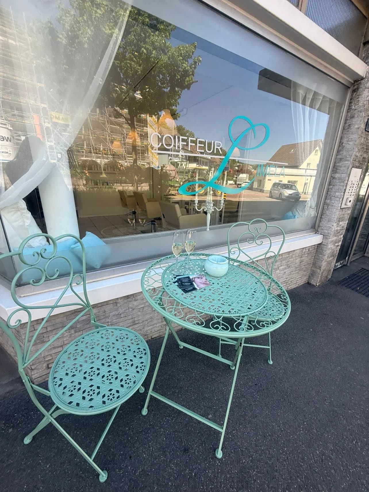 Das Schaufenster an der Aarauerstrasse mit dem tuerkisen Schriftzug Coiffeur Limela auf der Scheibe, davor ein mintfarbenes Bistrotischchen mit zwei Stuehlen.